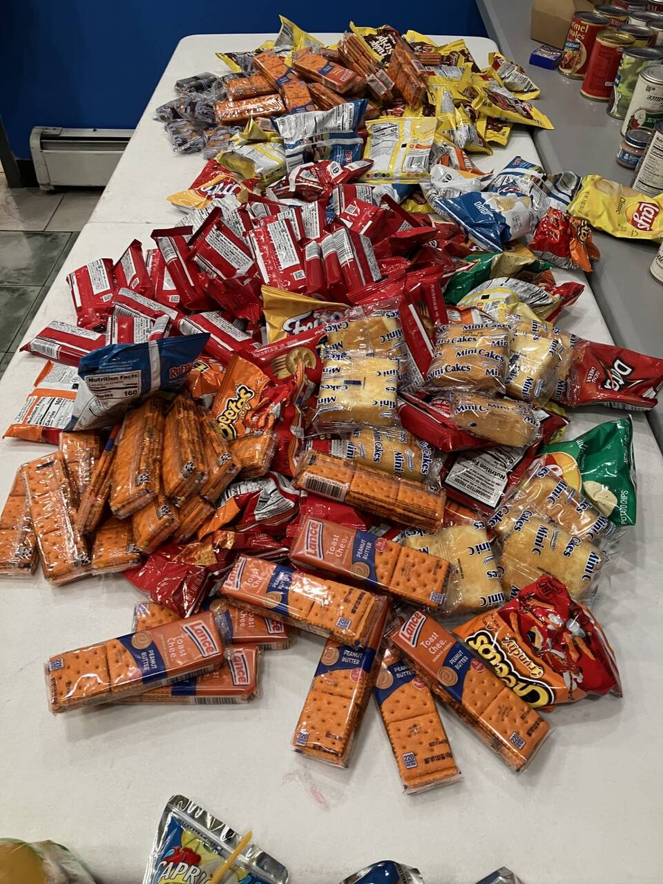 Snack table piled with chips, crackers, and mini cakes for guests